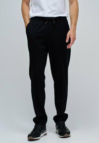 Pantalones jogger negros, ligeros, con cintura elástica, cordón, bolsillos laterales y un diseño de pierna ajustada. Textura suave y mate.