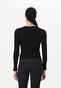 Hosszú ujjú fekete bordázott felső, testhezálló szabással, kerek nyakkivágással és sima textúrával, sötét denim farmernadrággal párosítva, amelynek hátsó zsebei vannak.