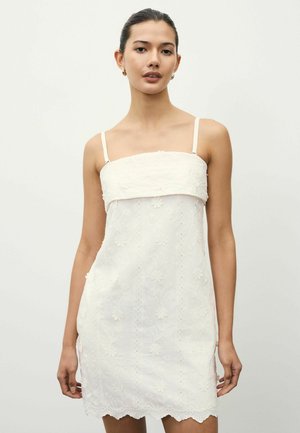 Robe blanche sans manches avec des motifs floraux brodés, ourlet festonné et corsage ajusté. Bretelles réglables, texture légère.