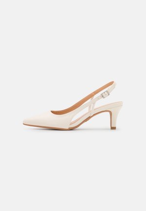 Creamfarvet slingback-pumpe med spids snude, lavt buet hæl og justerbar spænde-rem på ensfarvet baggrund.