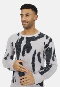 Pull en peluche gris clair avec des motifs abstraits noirs contrastés, doté d'un col rond et de manches longues avec une texture douce.