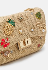Borsa a tracolla beige intrecciata con hardware dorato, decorata con abbellimenti colorati come un ananas, un granchio, una palma e un fiore di ibisco.