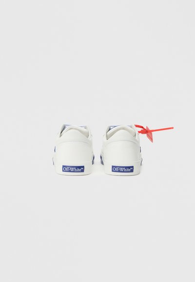 Fehér sportcipők kék részletekkel és márkajelzéssel a saroknál, a bal cipőn piros címkével. Simább anyag, alacsony szárú kialakítás.