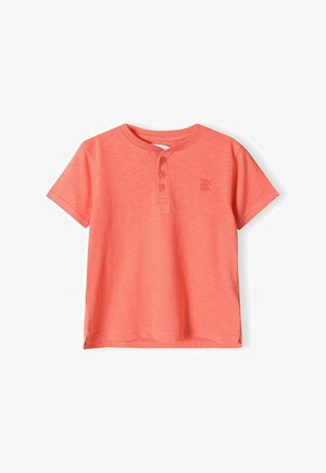 Korall színű, rövid ujjú pólóing, puha anyagból készült, három gombos gallérral és kis hímzett logóval a mellkasán.