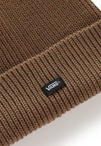 Gorro de punto marrón con textura acanalada, con una etiqueta negra de Vans cosida en el puño. Material suave, forma redondeada.