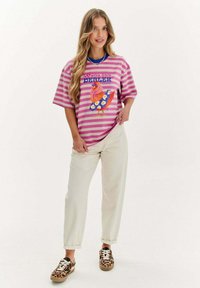 Růžové a bílé pruhované oversize tričko s barevným potiskem kuřete a textem, spárované s krémovými kalhotami a botami s leopardím vzorem.