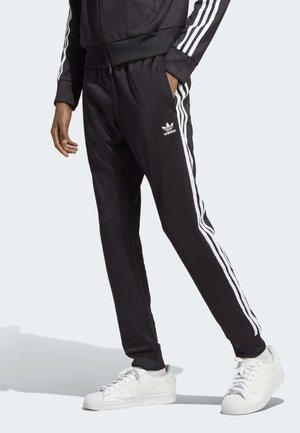 Pantaloni sportivi neri con strisce bianche ai lati e vita elastica, realizzati in tessuto morbido. Abbinati a sneaker bianche con tre strisce.