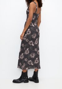 Vestido midi floral en gris oscuro con acentos rosas, con corsé fruncido y tirantes ajustables. Lleva botines negros.