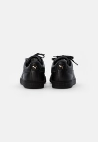 Zapatillas negras con parte superior de cuero, suela de goma texturizada y lengüetas alargadas. Presentan cordones a tono y un pequeño logo dorado en el talón.