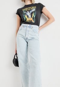 Camiseta gráfica negra con un diseño colorido que presenta una criatura mítica; combinada con unos jeans de tiro alto en azul claro con un ajuste relajado.