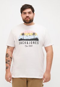 Hvid bomulds t-shirt med et farverigt grafisk motiv af palmetræer mod en solnedgang, med "JACK & JONES Est. 1990" trykt nedenunder.