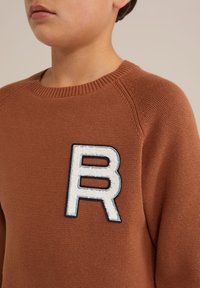 Maglione a maglia marrone con scollo rotondo, polsini a coste e un patch bianco con la lettera "R" bordato di blu navy.