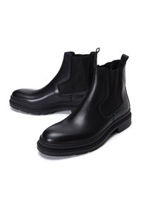 Bottines Chelsea en cuir noir avec des panneaux élastiques sur les côtés, bout rond, accents texturés, semelle en caoutchouc solide et languettes pour un enfilage facile.