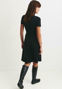 Sort kjole med korte ærmer, tætsiddende overdel, flydende skørter og snøre ved taljen. Kombineret med knælange sorte læderstøvler.