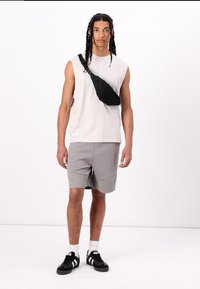 Sac à bandoulière noir, haut sans manches gris clair, shorts gris clair avec panneau texturé, et chaussures de sport noires avec rayures blanches.
