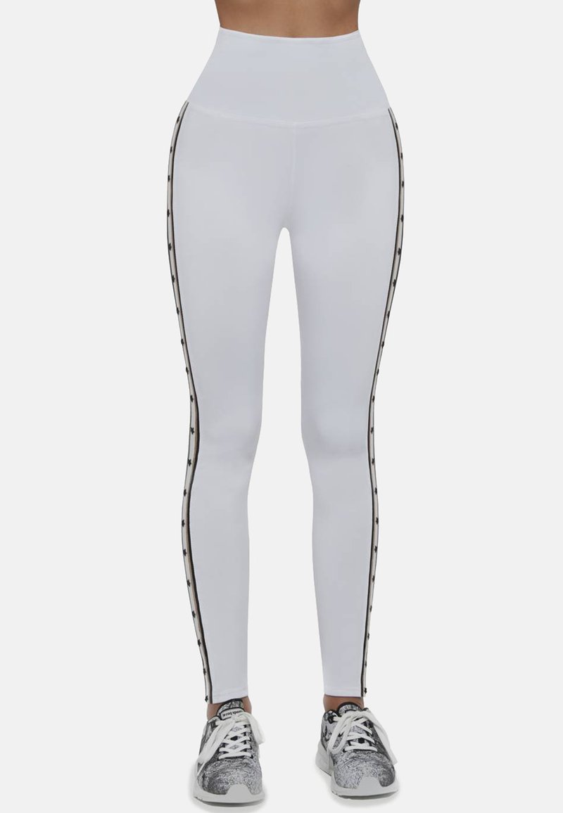 Białe legginsy z wysokim stanem, czarnymi paskami po bokach z akcentami i gładką fakturą. W połączeniu z wzorzystymi butami sportowymi.