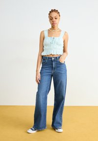 Lyst blå, stretchy crop top med samlet detaljer og firkantet halslinje, paret med høytlivde, vide blå jeans og hvite sneakers.
