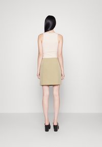 Haut sans manches rose clair et mini-jupe verte olive. La jupe présente une coupe droite et une fermeture éclair au dos. Mules noires à talons bloc.