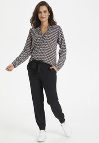Blusa a maniche lunghe in tessuto fantasia, bianco e nero, con scollatura a V. Pantaloni jogger neri con polsini elasticizzati e dettaglio in vita con cintura. Sneakers bianche.