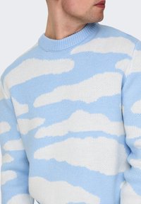 Lyseblå strikket sweater med et sky-mønster i hvid. Designet inkluderer en ribbet halsudskæring og struktureret stof.