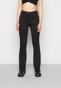 As calças pretas com boca de sino apresentam uma textura suave, cintura alta e detalhes vermelhos nos bolsos laterais. Projetadas para uma silhueta ajustada.