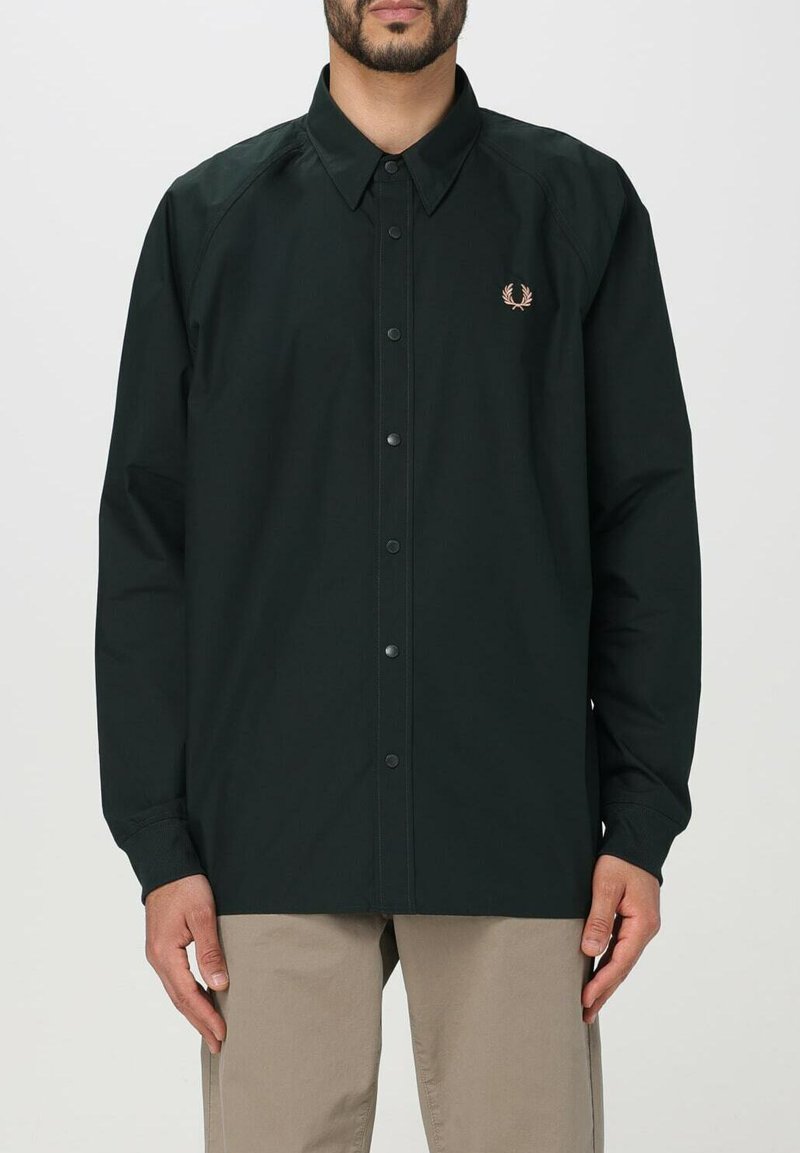 Camicia a maniche lunghe verde scuro con colletto a punta, dotata di un piccolo logo ricamato sul petto e bottoni a pressione lungo la parte anteriore.