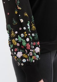 Μαύρο φούτερ με πολύχρωμη κεντητή λουλουδάτη διακόσμηση σε ροζ, κίτρινο και πράσινο, με ελαστικά μανσέτες και απαλή υφή.