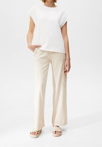 Witte katoenen T-shirt met korte mouwen, gecombineerd met lichtbeige wijde broek met zakken. Tan platform sandalen maken de outfit compleet.