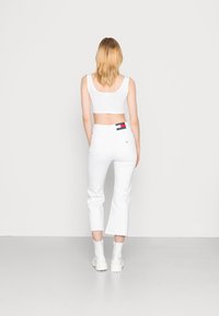 Top corto blanco y jeans acampanados blancos de cintura alta con dobladillos sin acabar. Modelo vistiendo botas blancas hasta el tobillo, vista desde atrás.