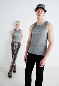 Gray ribbed tank tops with "A gift from God" text, paired with patterned pants. One model wears a gray cap; others have chunky patterned shoes.