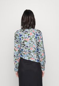 Floral long-sleeve blouse featuring a light blue background with multicolored flower patterns and a relaxed fit, paired with a black skirt.