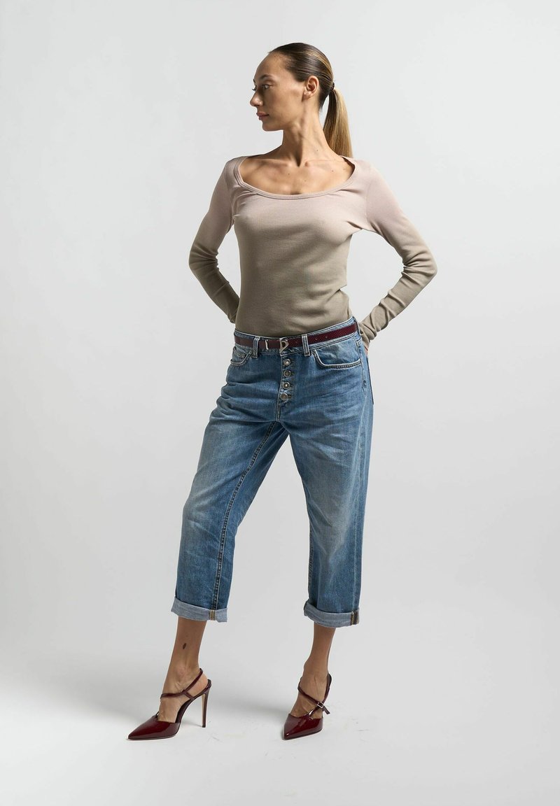 Top a maniche lunghe beige a costine, jeans blu a vita alta con risvolti e décolleté rosse con punta, che mostrano una silhouette aderente e accenti a contrasto.