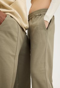 Olive green sweatpants with elastic waistband and side pockets, featuring visible stitching and a soft, textured fabric.