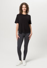 Maglietta nera a maniche corte abbinata a leggings grigio scuro e sneakers bianche, presentando una combinazione casual di materiali e colori.