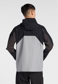 Grijze en zwarte capuchonjack met een contrasterend paneelontwerp, een zachte textuur en elastische manchet, geschikt voor buitensportactiviteiten.