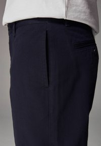 Pantalon bleu marine en tissu mélangé de coton, avec une texture lisse, poche latérale et un subtil détail de couture à la taille.