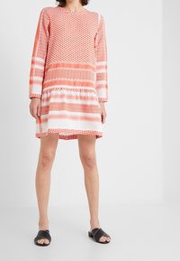 Vestido de manga larga, a la altura de la rodilla, en naranja y blanco con lunares y patrones de zigzag. Tejido texturizado con fruncidos en el dobladillo.