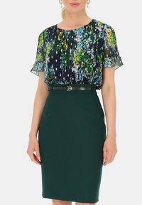 Bluzka we wzór kwiatowy z krótkimi, przezroczystymi rękawami, w połączeniu z dopasowaną, ciemnozieloną spódnicą ołówkową oraz pasującym paskiem z srebrną klamrą.