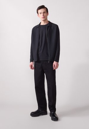 Zwarte zip-up jack over een zwart T-shirt, gecombineerd met zwarte broek en stevige zwarte laarzen, met een gestructureerde stof en klassieke silhouet.