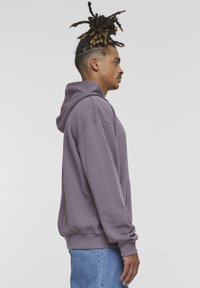 Felpa viola con cappuccio, tasca frontale, vestibilità comoda, polsini e orlo a costine. Abbinata a jeans in denim blu chiaro.