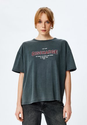 Mørkegrå oversized t-shirt med korte ærmer, prydet med hvid og rød tekst med teksten "DISCHARGE." Blødt stof med en afslappet pasform.