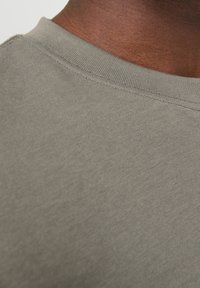 Šedé bavlněné tričko s kulatým výstřihem, které má hladkou, jednobarevnou texturu a malé švy kolem límce.