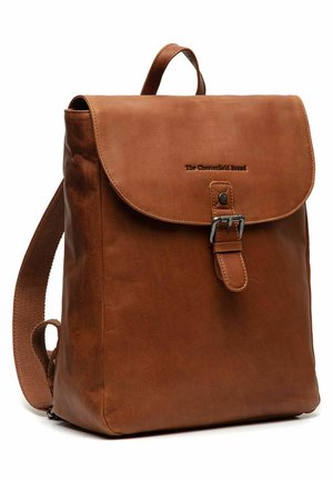 Sac à dos en cuir marron avec une fermeture à rabat, une boucle en métal et des bretelles en tissu réglables. Il présente une texture lisse et un logo estampé sur le devant.