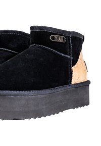 Botines de ante negro con un acento de corcho, superficie texturizada y una suela de goma negra gruesa en contraste. Presenta una etiqueta metálica de la marca.