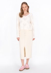Häkelstrickpullover in Creme mit Rautenmuster, kombiniert mit einem beigen Midikleid mit Schlitz vorne und rosa Turnschuhen.