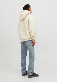 Felpa con cappuccio in pile color crema con superficie texturizzata, cappuccio e orlo a costine. Abbinata a jeans azzurri e scarpe da ginnastica scure.