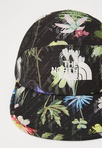 Svart cap med mønster som har blomsterdesign i livlige farger. Inkluderer "THE NORTH FACE" logo i hvitt på foran. Laget av teksturert stoff.