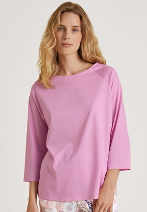Top rosa chiaro a maniche lunghe con scollatura arrotondata e maniche raglan, realizzato in tessuto morbido, abbinato a pantaloni leggeri a fantasia.