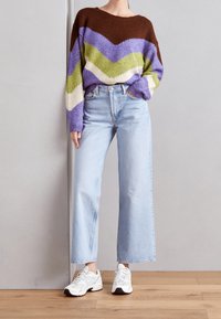 Person wearing light blue wide-leg jeans, white sneakers, and a colorful chevron-patterned sweater with brown, purple, green, and white stripes.