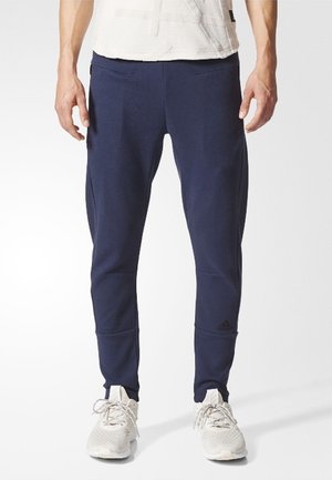 Granatowe joggery wykonane z miękkiego materiału, z tapered designem, bocznymi kieszeniami i logo Adidas na dolnej części nogawki.